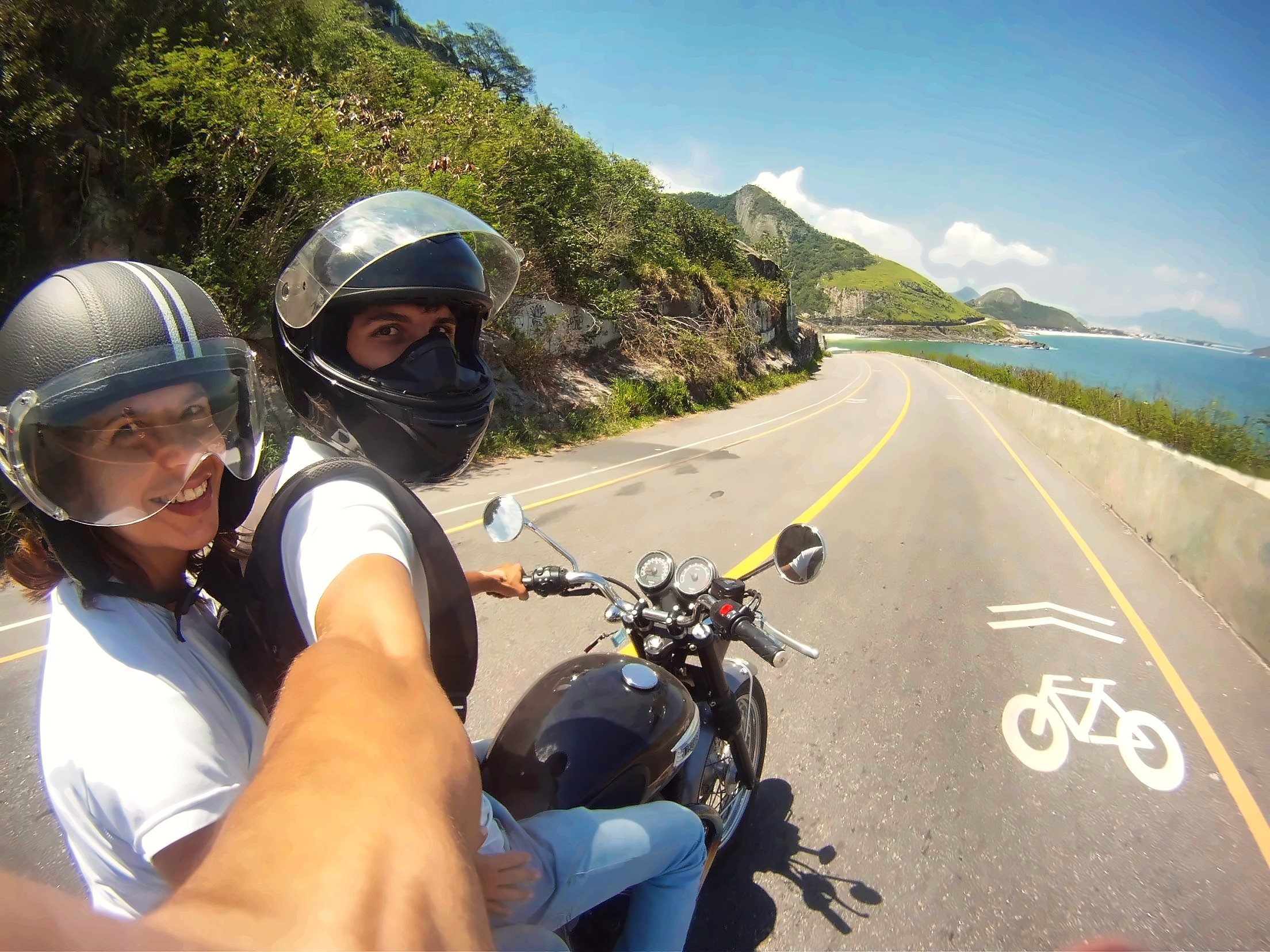 Passenger riding pillion with an Xplore guide on a coastal road