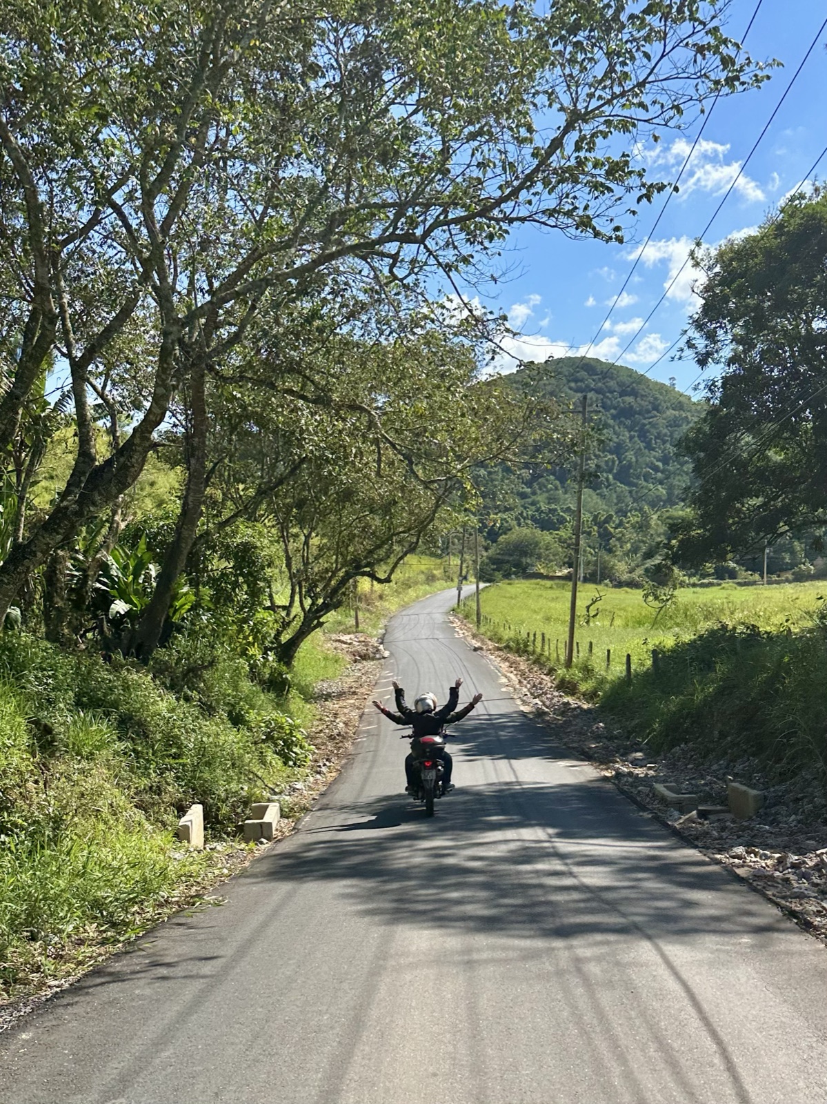 Pasajera y guía con los brazos en alto en una tranquila carretera rural, con colinas al frente