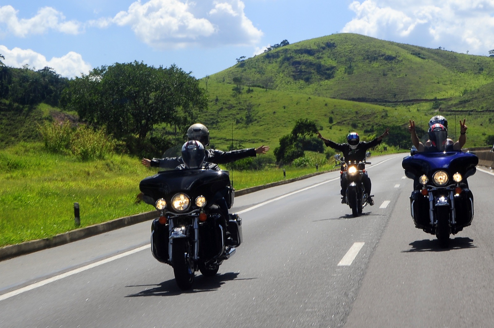 Sozia mit weit ausgebreiteten Armen auf einem Tourenmotorrad, umgeben von grünen Hügeln