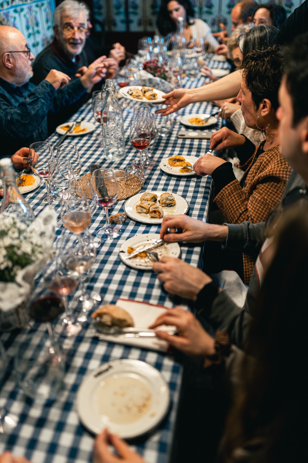 A long table with blue checked cloths, plates of food and glasses of wine
