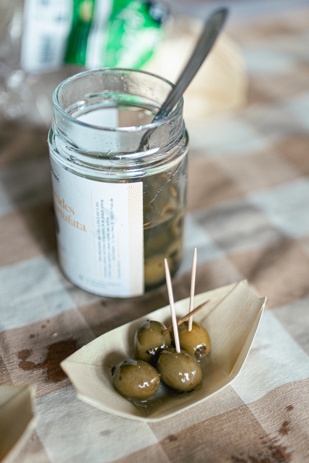 Truffled olives on toothpicks in a small paper boat, the jar behind them