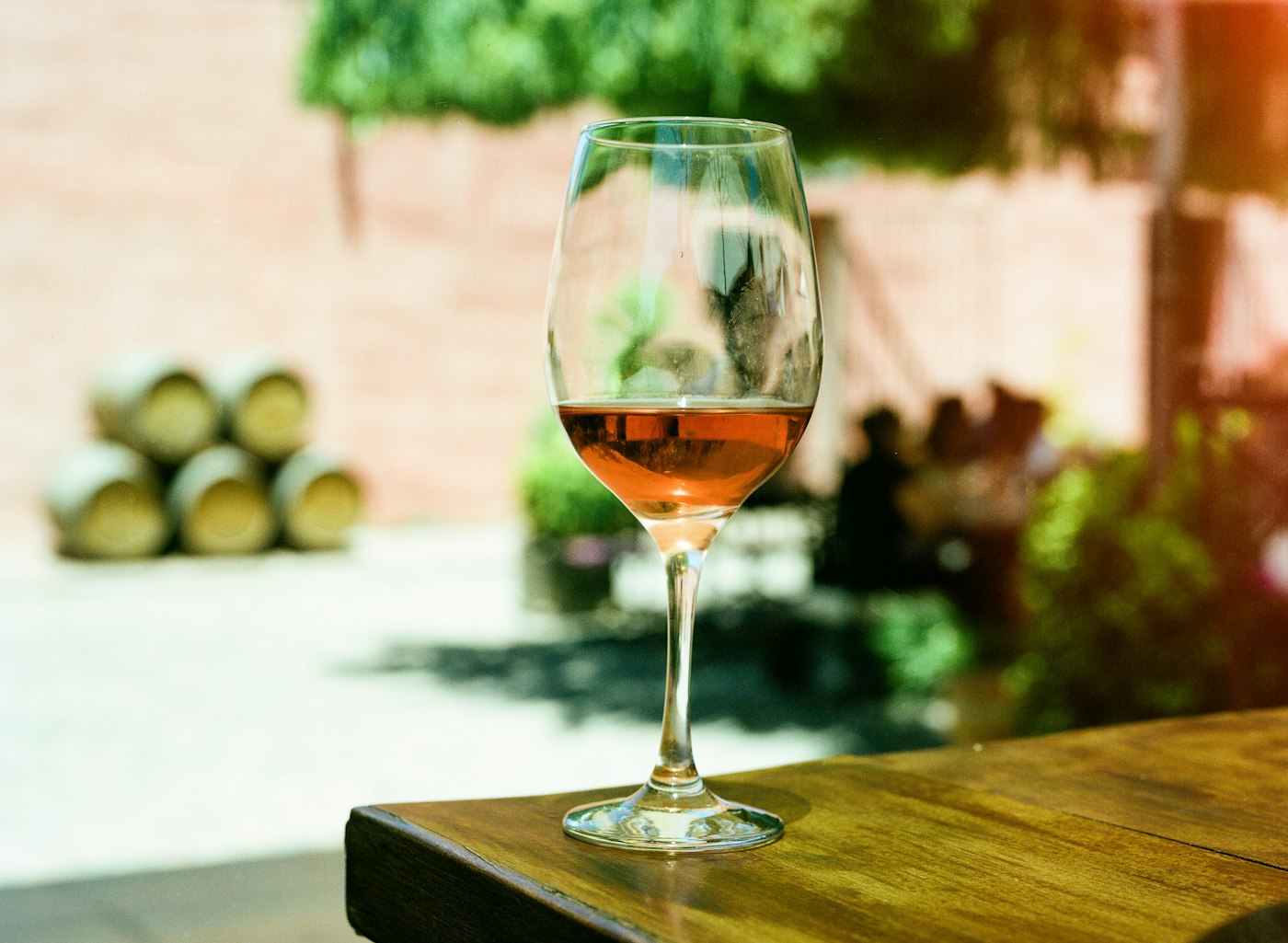 A glass of ros&eacute; on a wooden table outdoors, in the sun