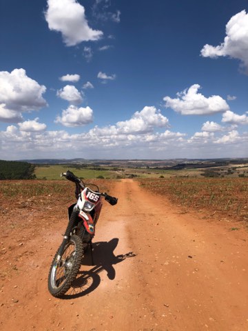 Rote Erdpiste durch offenes Farmland unter hohen Wolken, Brasilien