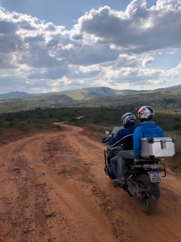 Deux personnes à moto sur une piste de terre rouge, les collines du sud du Minas Gerais derrière