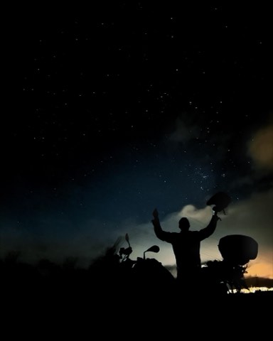 Pilote en silhouette à côté d'une moto sous un ciel rempli d'étoiles à Carrancas