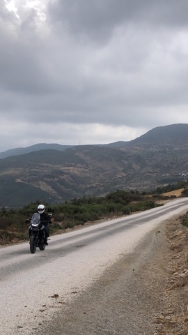 Motorcycle on a narrow road through dry hills in Morocco under an overcast sky