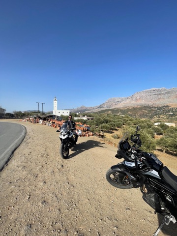 Two adventure motorcycles parked beside a roadside village with a white minaret in the Moroccan mountains