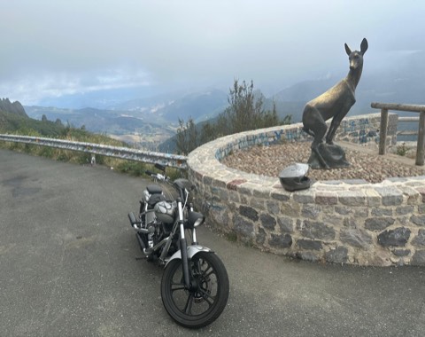 Chopper parked at a stone viewpoint with a bronze deer, cloud filling the valley below