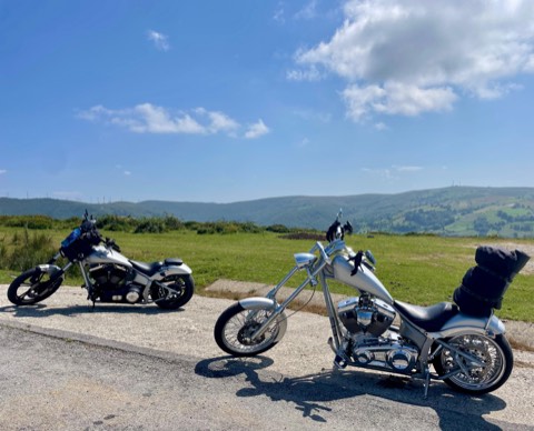 Two choppers parked side by side on a verge with green Cantabrian hills behind