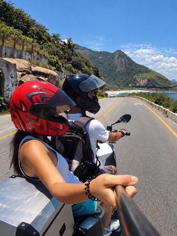Passenger and pilot on a motorcycle on the coast road in Rio de Janeiro, with the ocean on the right